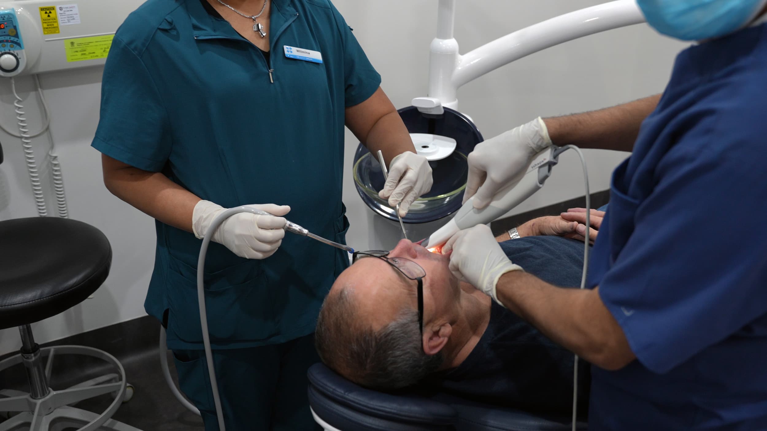 Dentist performing dental filling treatment with assistant supporting patient.