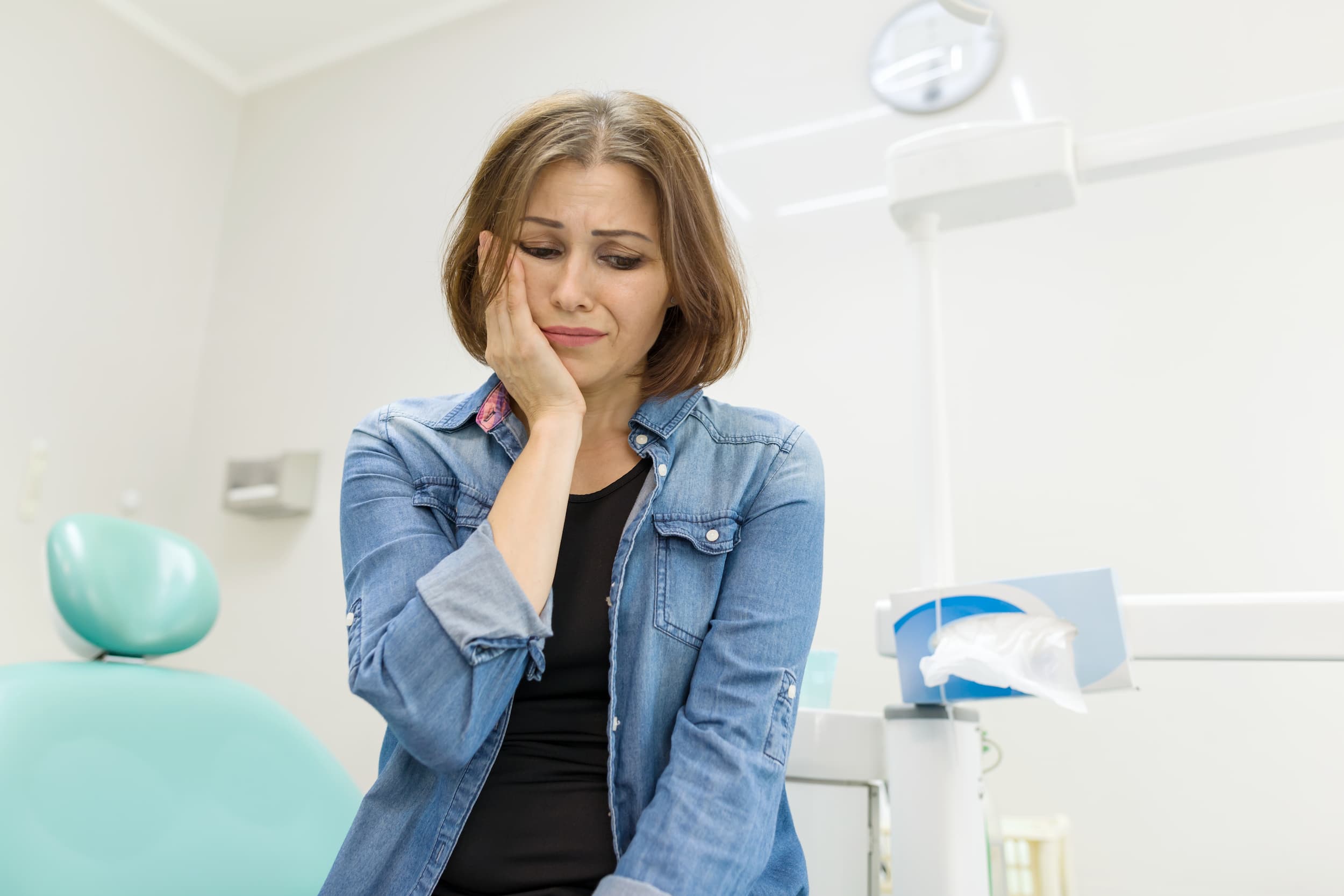 Woman holding her jaw in pain while seated in a dental clinic.